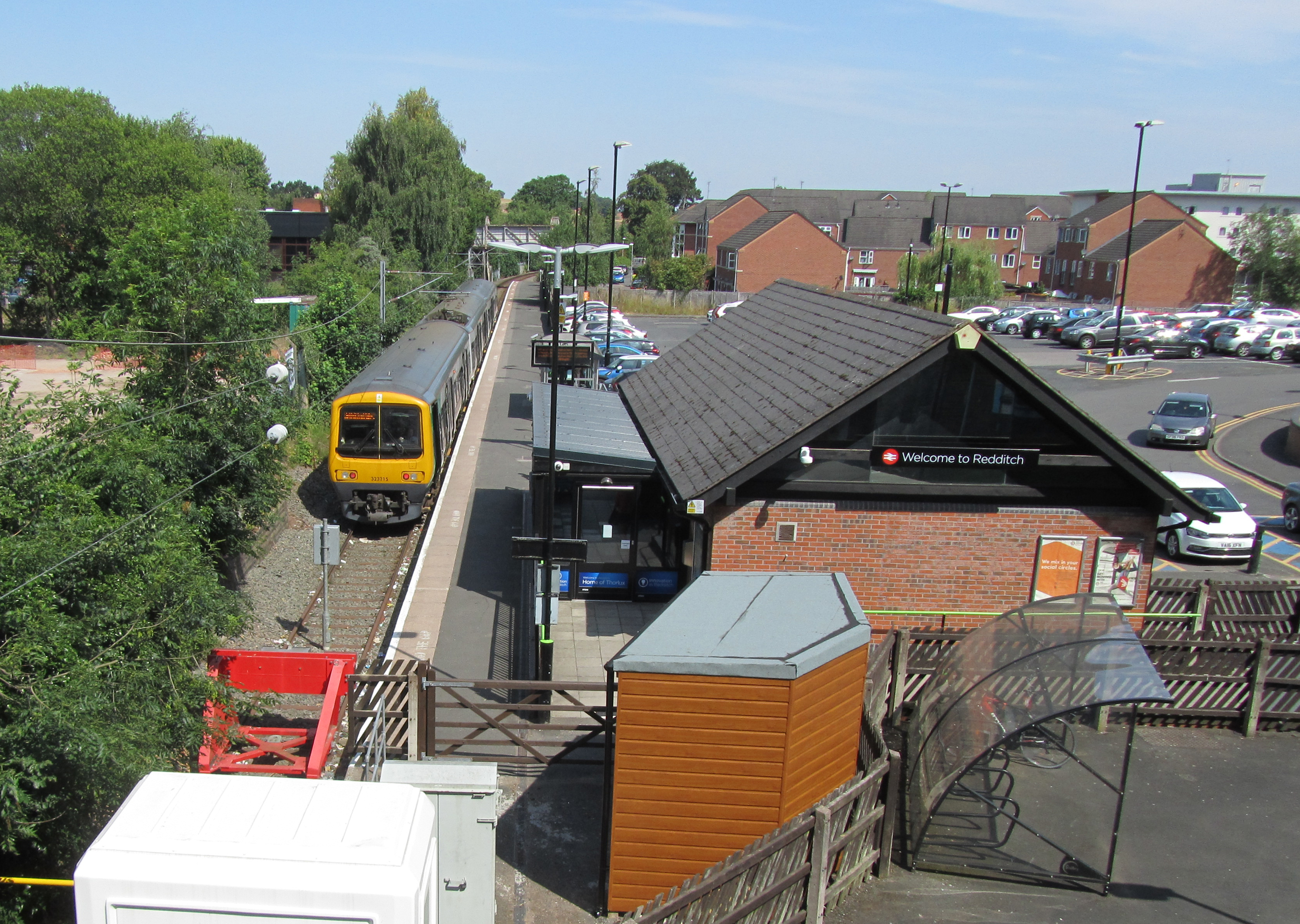 Railway station and tracks bordered by trees lining the tracks, with the train station building and platform opposite.